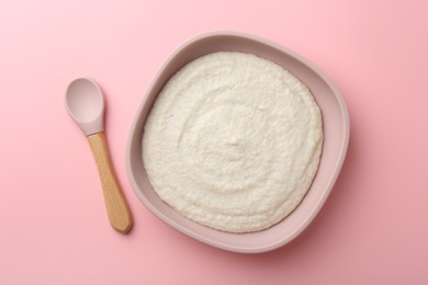 Photo of Delicious baby food in bowl and spoon on pink background, top view