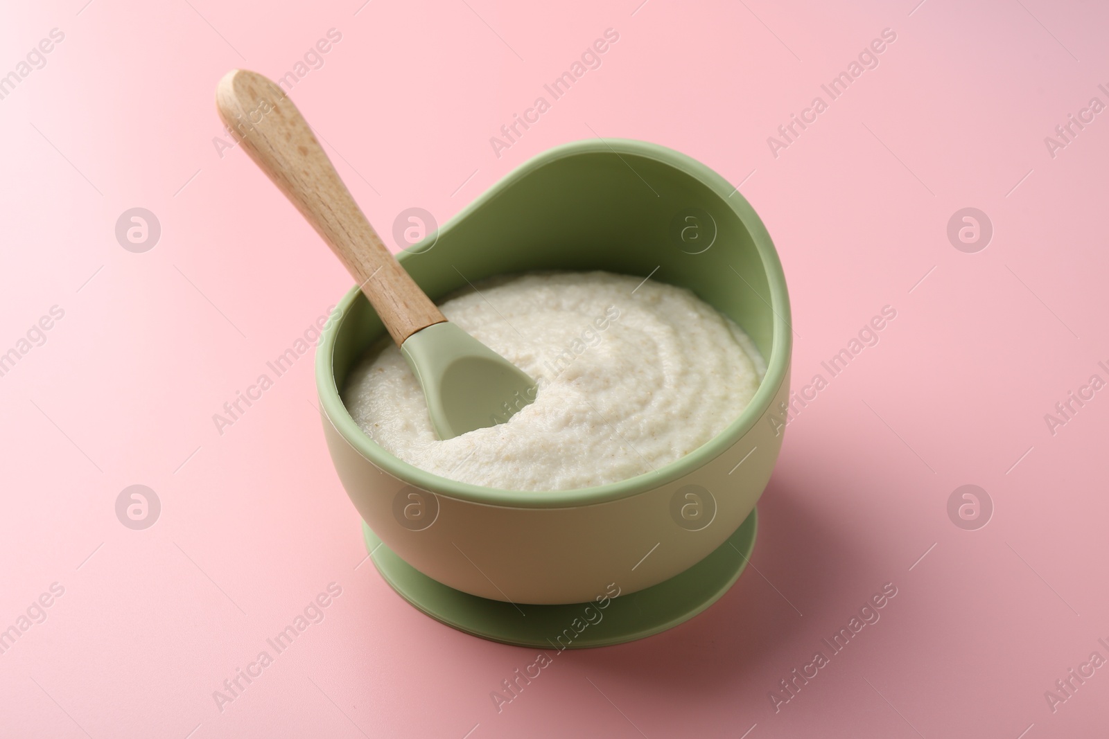 Photo of Delicious baby food in bowl and spoon on pink background