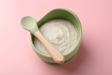 Photo of Delicious baby food in bowl and spoon on pink background