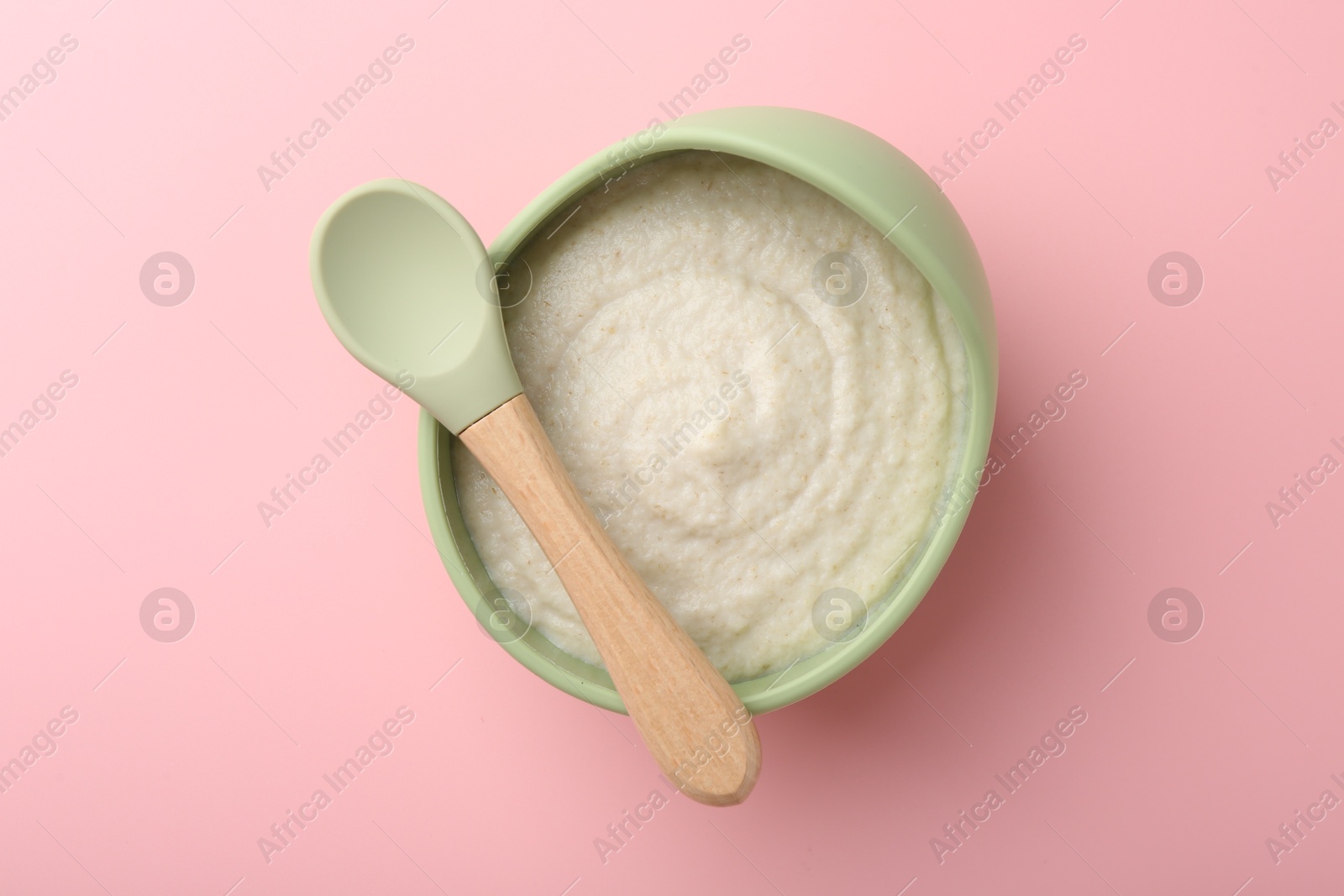 Photo of Delicious baby food in bowl and spoon on pink background, top view