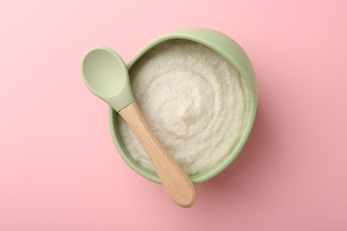 Photo of Delicious baby food in bowl and spoon on pink background, top view