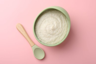 Photo of Delicious baby food in bowl and spoon on pink background, top view