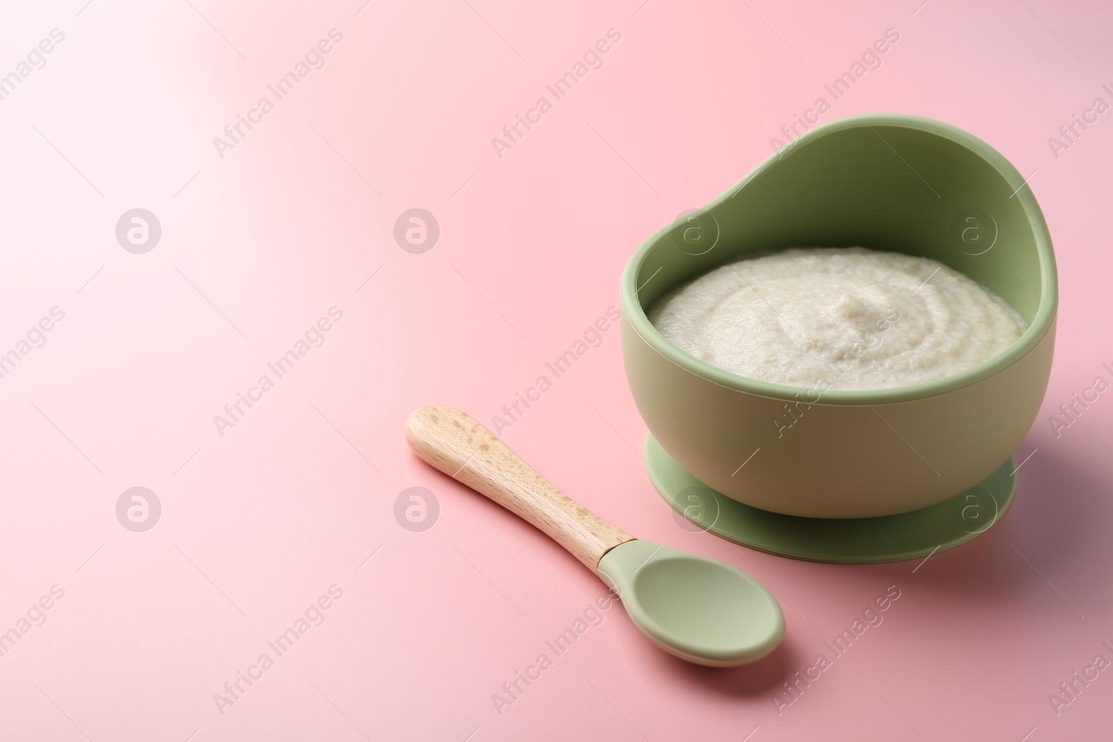 Photo of Delicious baby food in bowl and spoon on pink background. Space for text