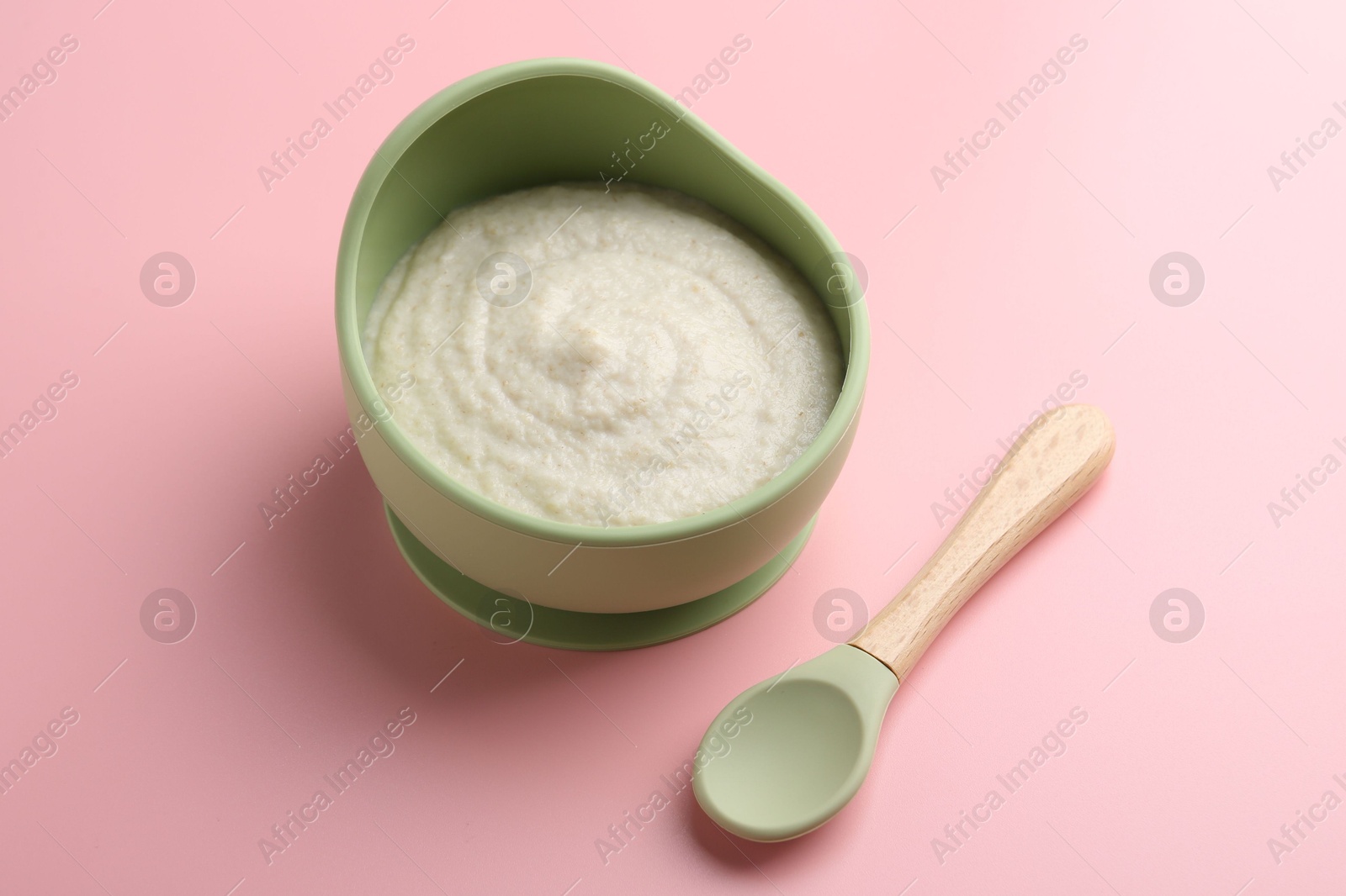 Photo of Delicious baby food in bowl and spoon on pink background