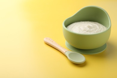 Photo of Delicious baby food in bowl and spoon on yellow background. Space for text