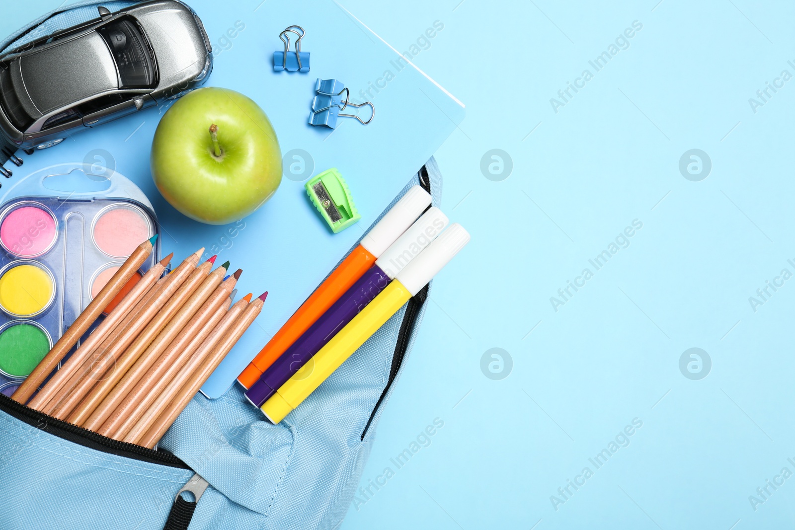 Photo of Backpack with different school stationery on light blue background, top view. Space for text