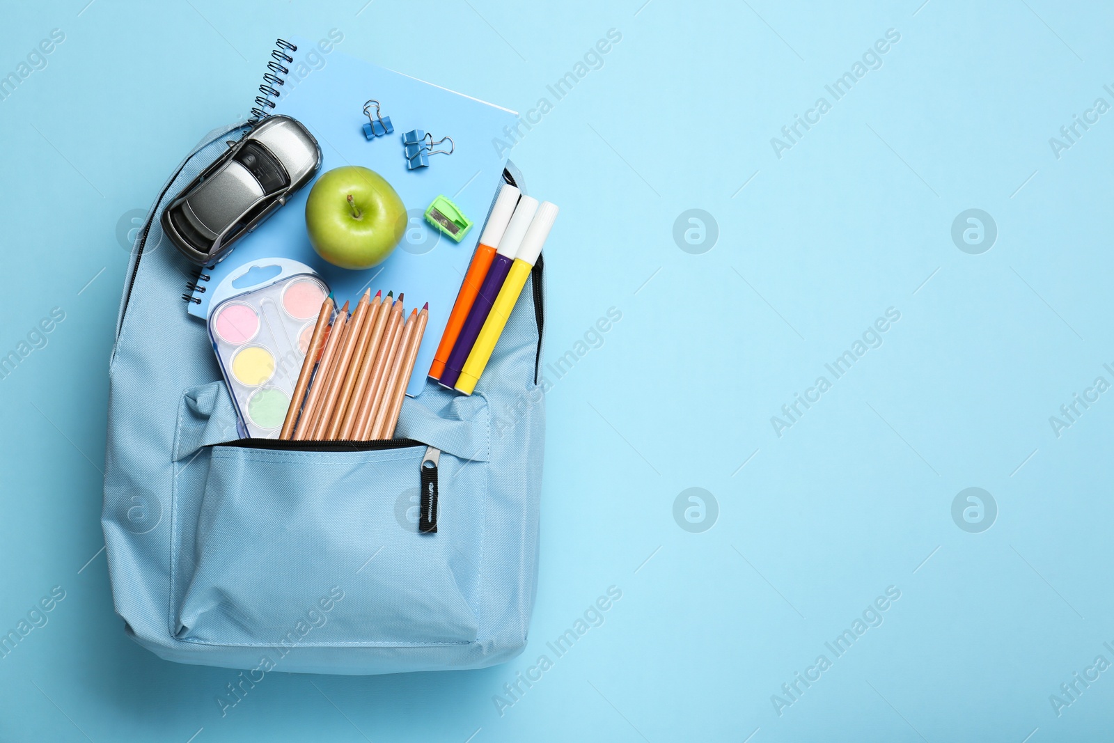 Photo of Backpack with different school stationery on light blue background, top view. Space for text