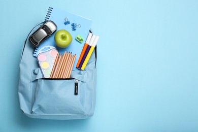 Backpack with different school stationery on light blue background, top view. Space for text