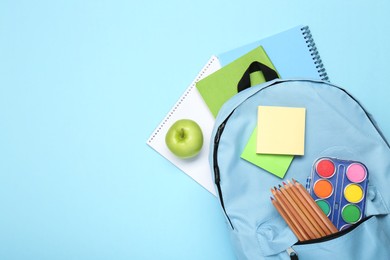 Photo of Backpack with different school stationery on light blue background, flat lay. Space for text