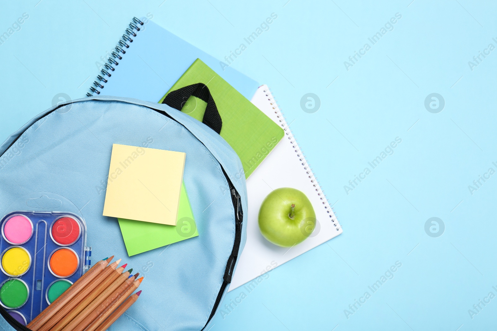 Photo of Backpack with different school stationery on light blue background, flat lay. Space for text