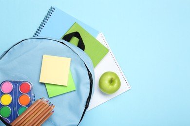 Photo of Backpack with different school stationery on light blue background, flat lay. Space for text