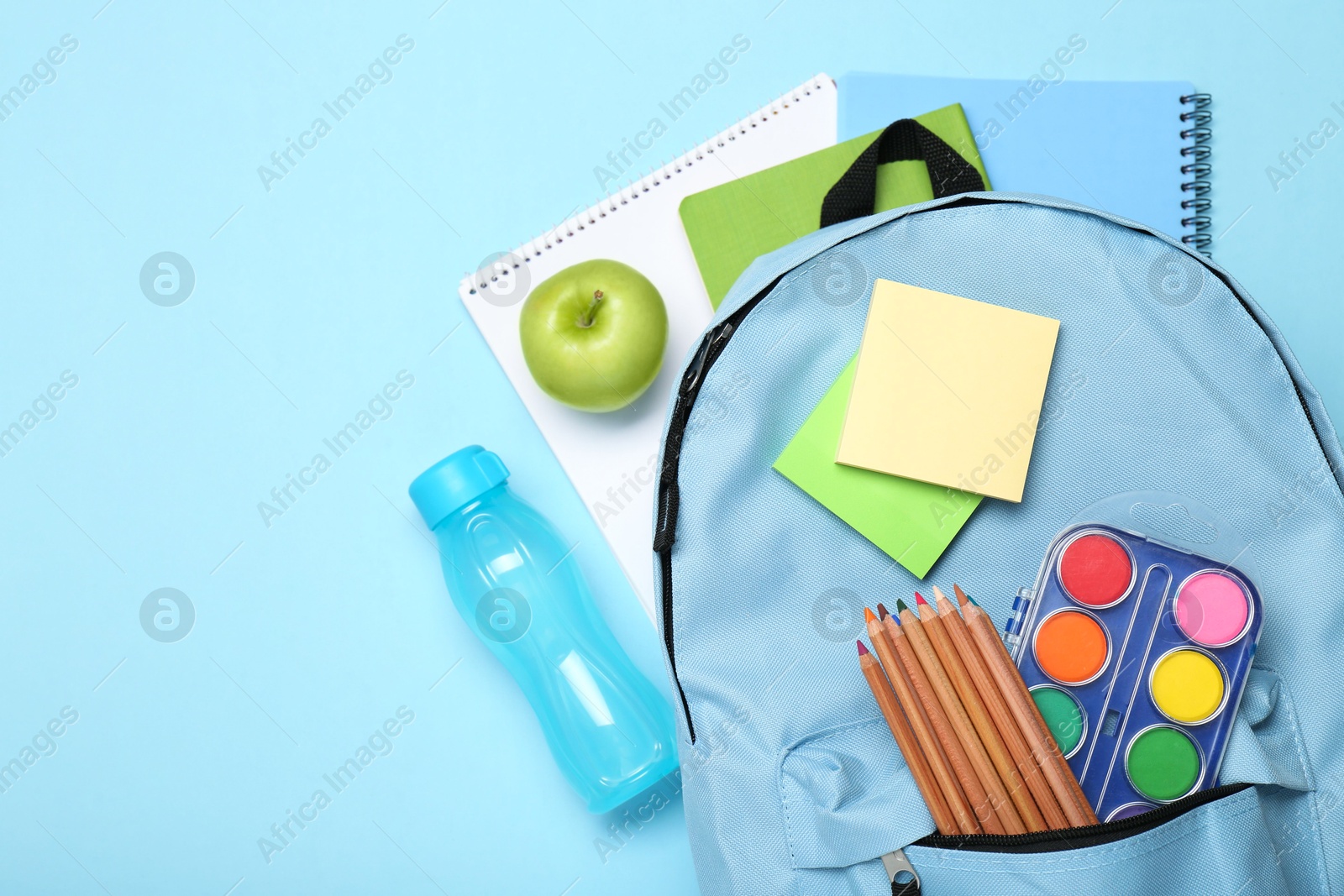 Photo of Backpack with different school stationery on light blue background, flat lay. Space for text