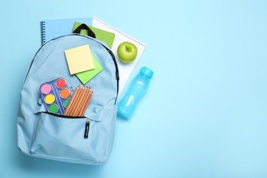 Photo of Backpack with different school stationery on light blue background, flat lay. Space for text