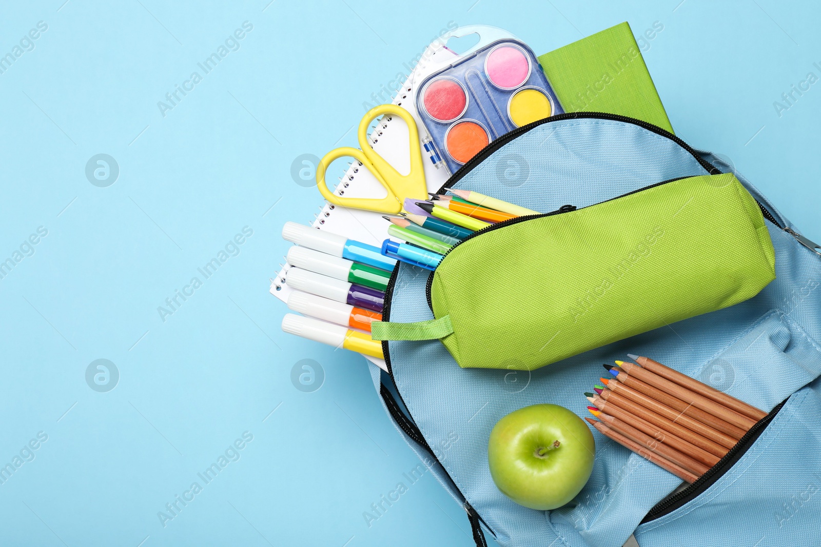 Photo of Backpack with different school stationery on light blue background, top view. Space for text