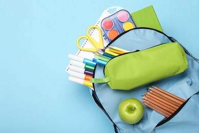 Photo of Backpack with different school stationery on light blue background, top view. Space for text