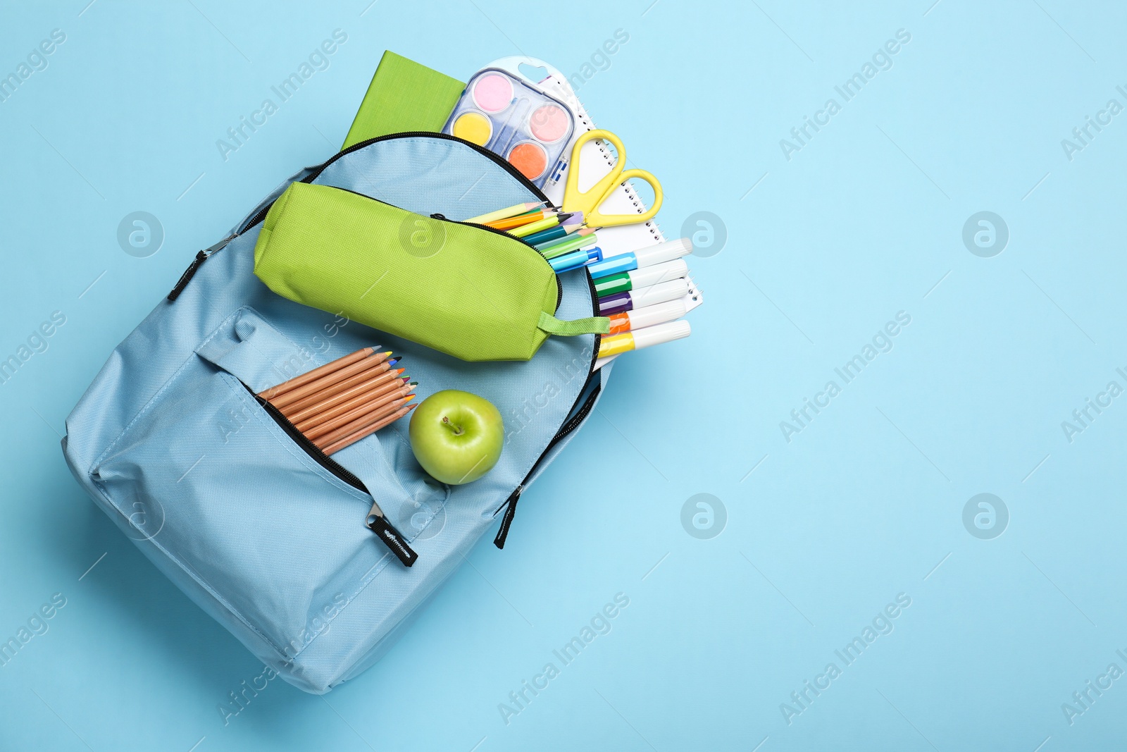 Photo of Backpack with different school stationery on light blue background, top view. Space for text