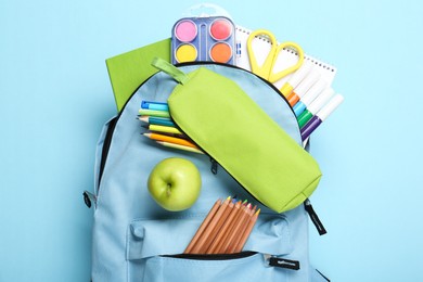 Photo of Backpack with different school stationery on light blue background, top view