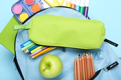 Backpack with different school stationery on light blue background, top view