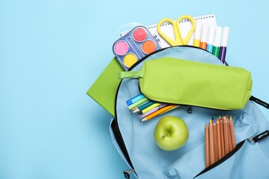 Photo of Backpack with different school stationery on light blue background, top view. Space for text