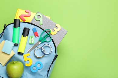 Photo of Light blue school backpack with stationery on green background, top view. Space for text