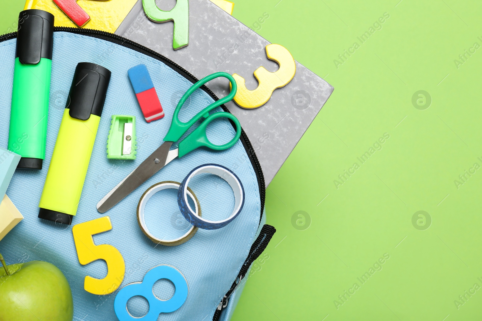 Photo of Light blue school backpack with stationery on green background, top view. Space for text