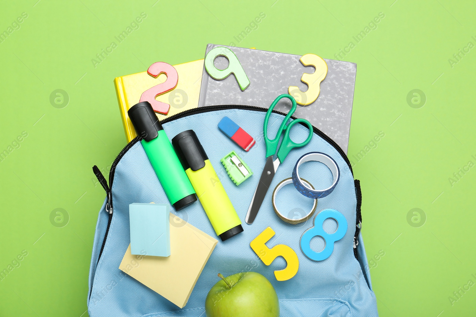 Photo of Light blue school backpack with stationery on green background, top view