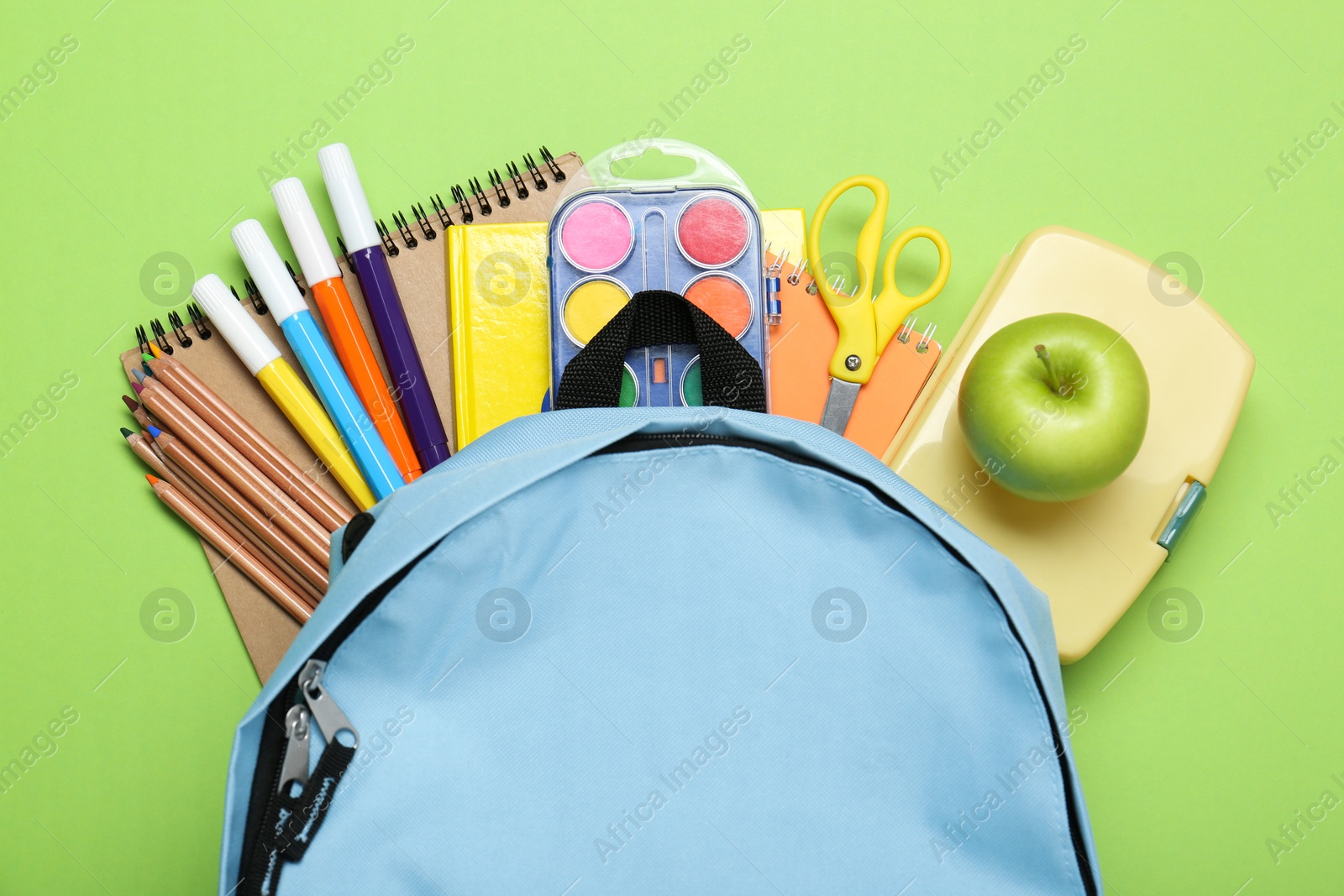 Photo of Light blue school backpack with stationery on green background, top view