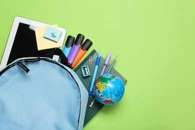 Photo of Light blue school backpack with stationery on green background, top view. Space for text