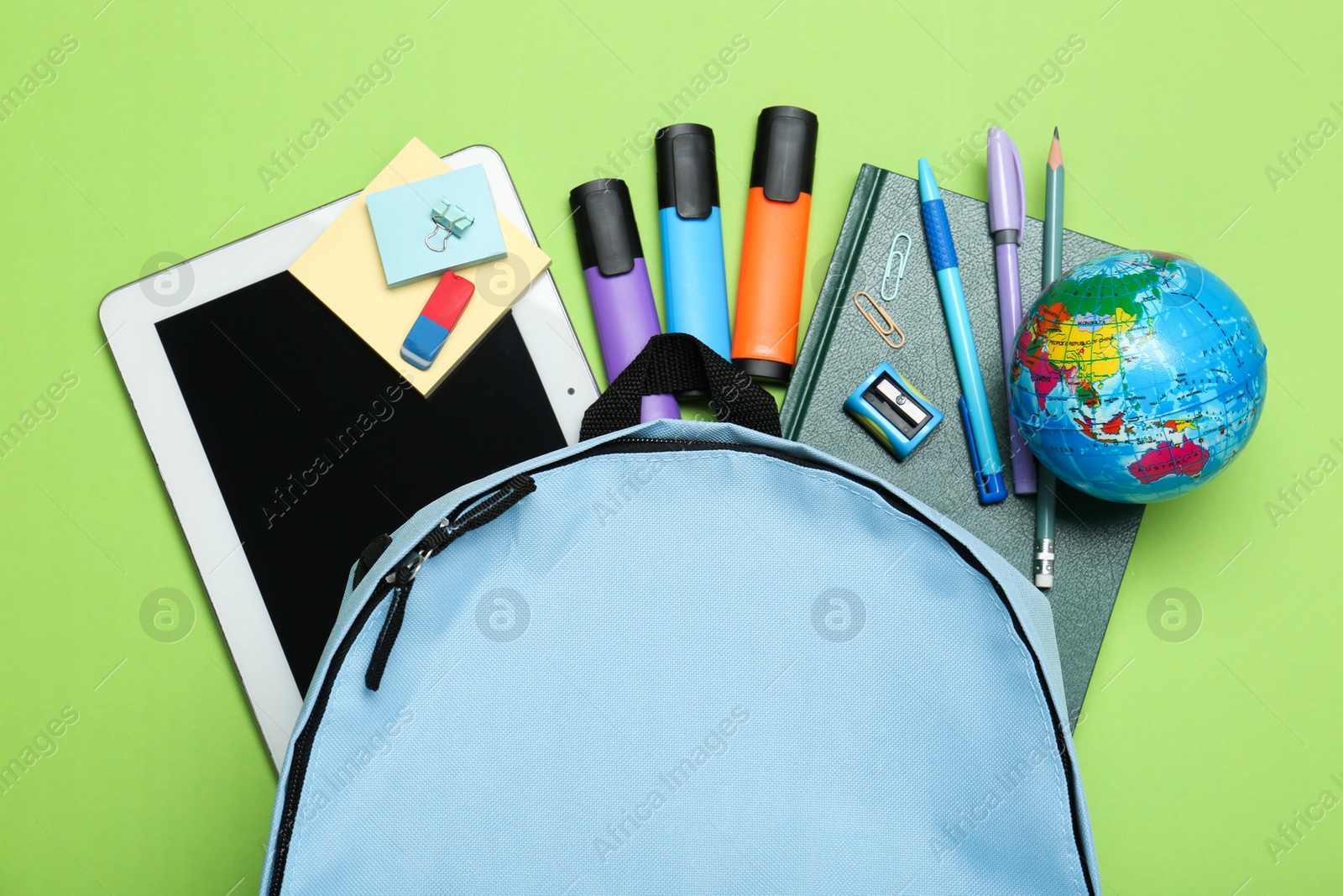 Photo of Light blue school backpack with stationery on green background, top view