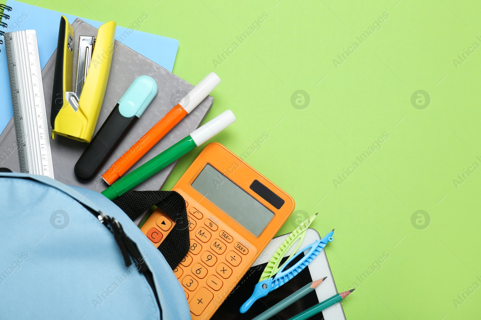 Photo of Light blue school backpack with stationery on green background, top view. Space for text