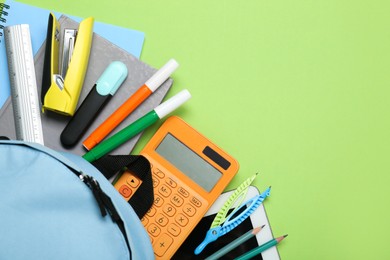 Photo of Light blue school backpack with stationery on green background, top view. Space for text