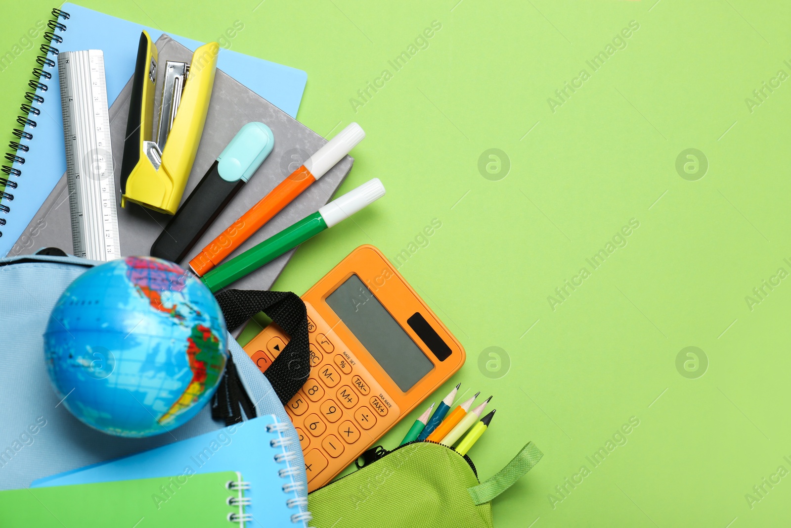 Photo of Light blue school backpack with stationery on green background, top view. Space for text