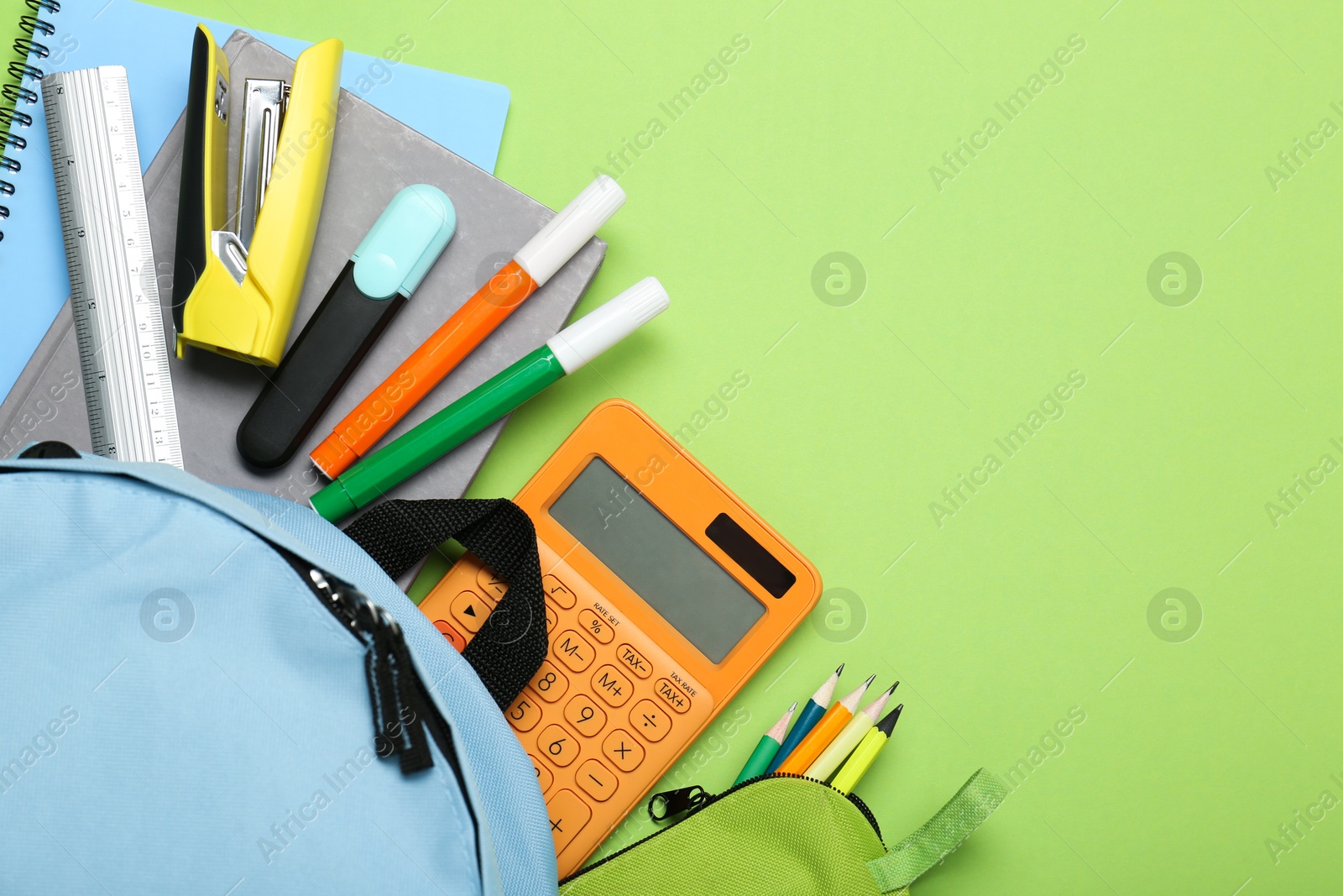 Photo of Light blue school backpack with stationery on green background, top view. Space for text