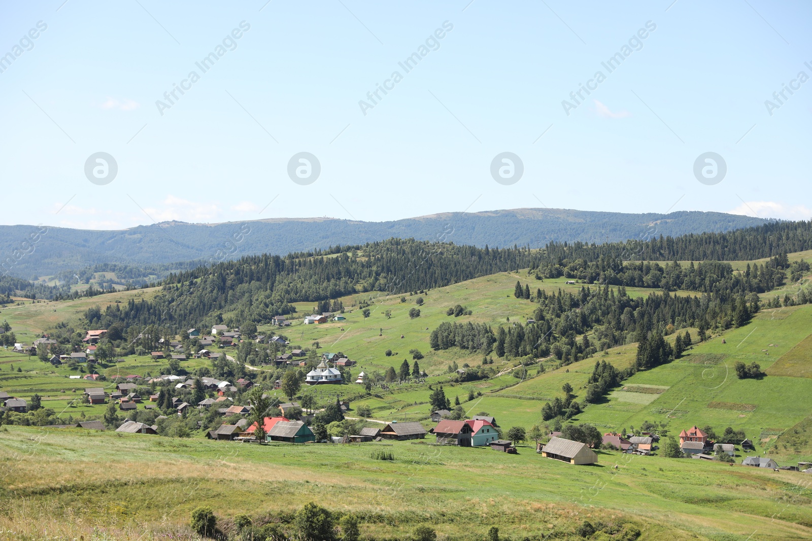 Photo of Picturesque view of houses and forest in mountains under blue sky