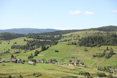 Photo of Picturesque view of houses and forest in mountains under blue sky