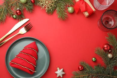 Photo of Beautiful Christmas setting with plate, elegant cutlery and festive decor on red table, flat lay. Space for text