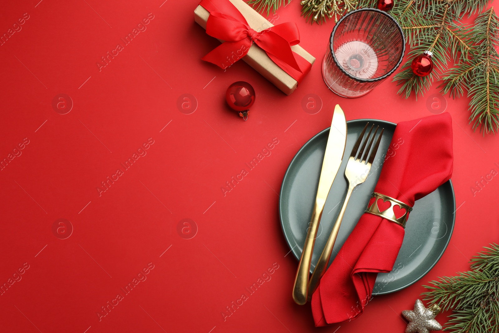 Photo of Beautiful Christmas setting with plate, elegant cutlery and festive decor on red table, flat lay. Space for text