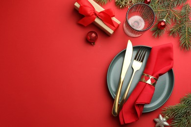 Photo of Beautiful Christmas setting with plate, elegant cutlery and festive decor on red table, flat lay. Space for text