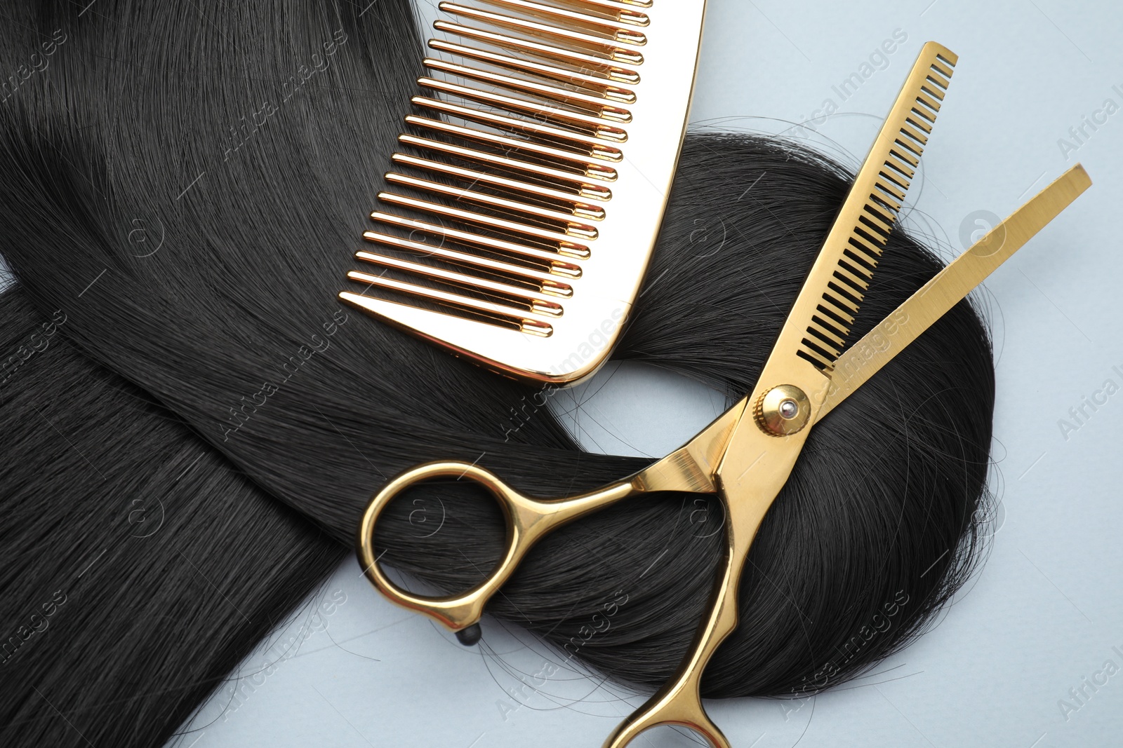 Photo of Black hair strand, comb and professional scissors on light grey background, top view