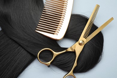 Black hair strand, comb and professional scissors on light grey background, top view