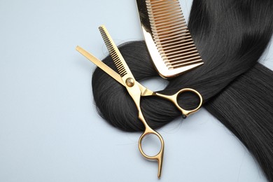 Black hair strand, comb and professional scissors on light grey background, top view