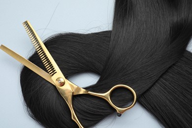 Photo of Black hair strand and professional scissors on light grey background, top view