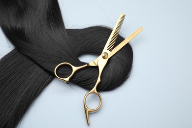 Photo of Black hair strand and professional scissors on light grey background, top view