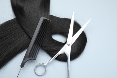 Photo of Black hair strand, comb and professional scissors on light grey background, top view