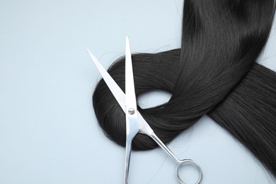 Black hair strand and professional scissors on light grey background, top view