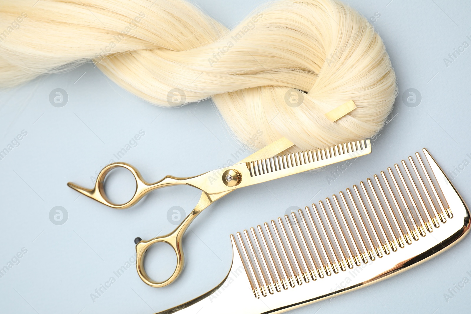 Photo of Blonde hair strand, comb and professional scissors on light grey background, top view