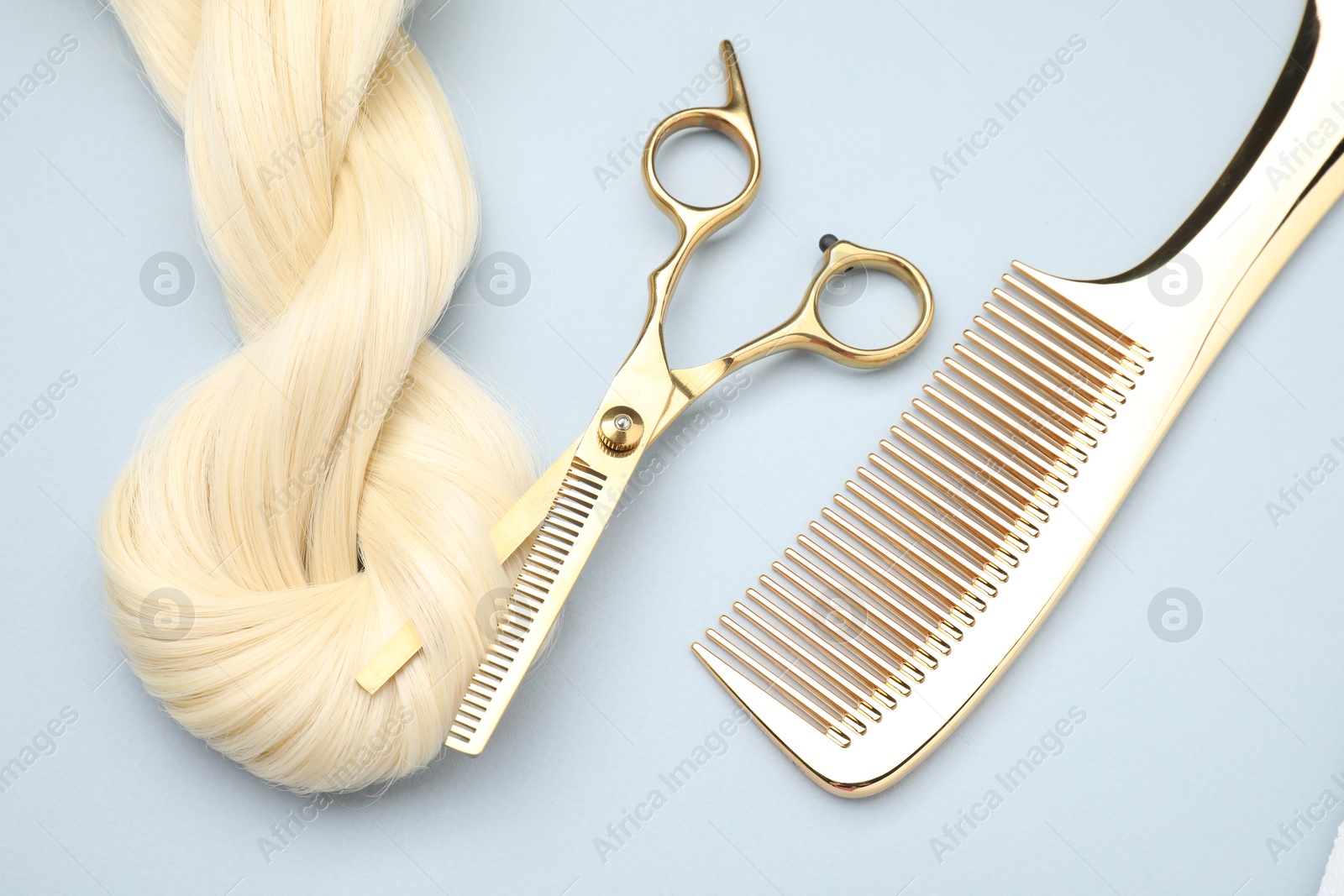 Photo of Blonde hair strand, comb and professional scissors on light grey background, top view