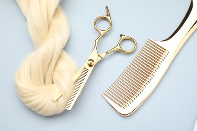 Photo of Blonde hair strand, comb and professional scissors on light grey background, top view