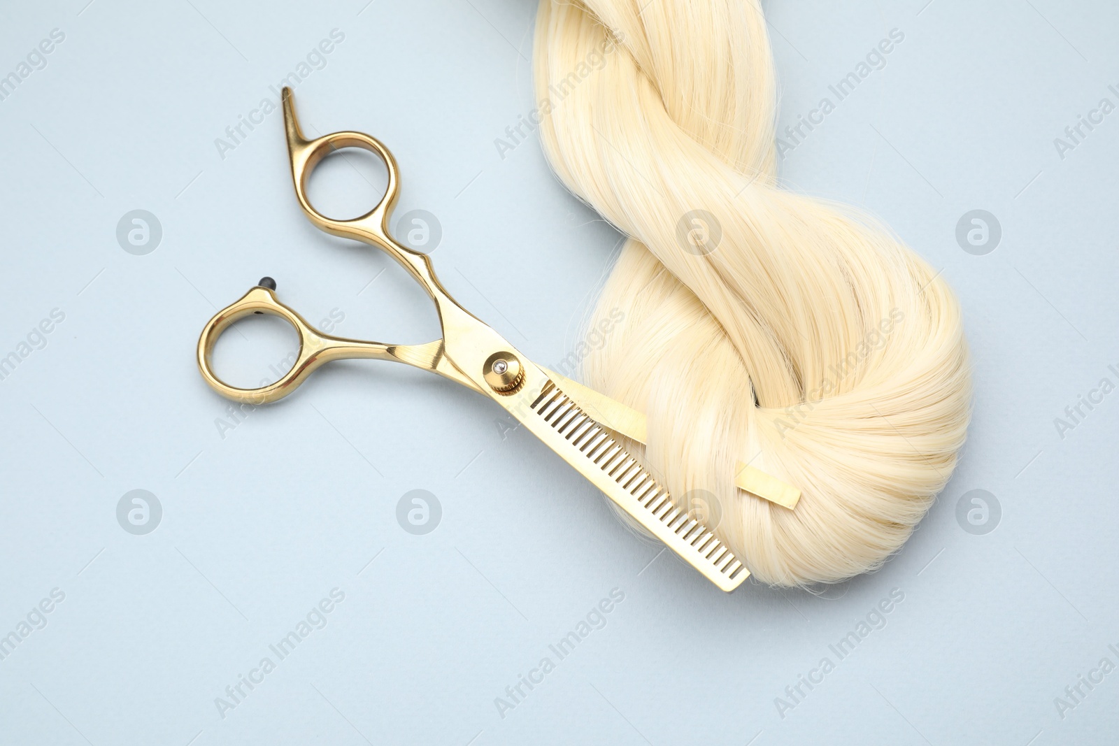 Photo of Blonde hair strand and professional scissors on light grey background, top view