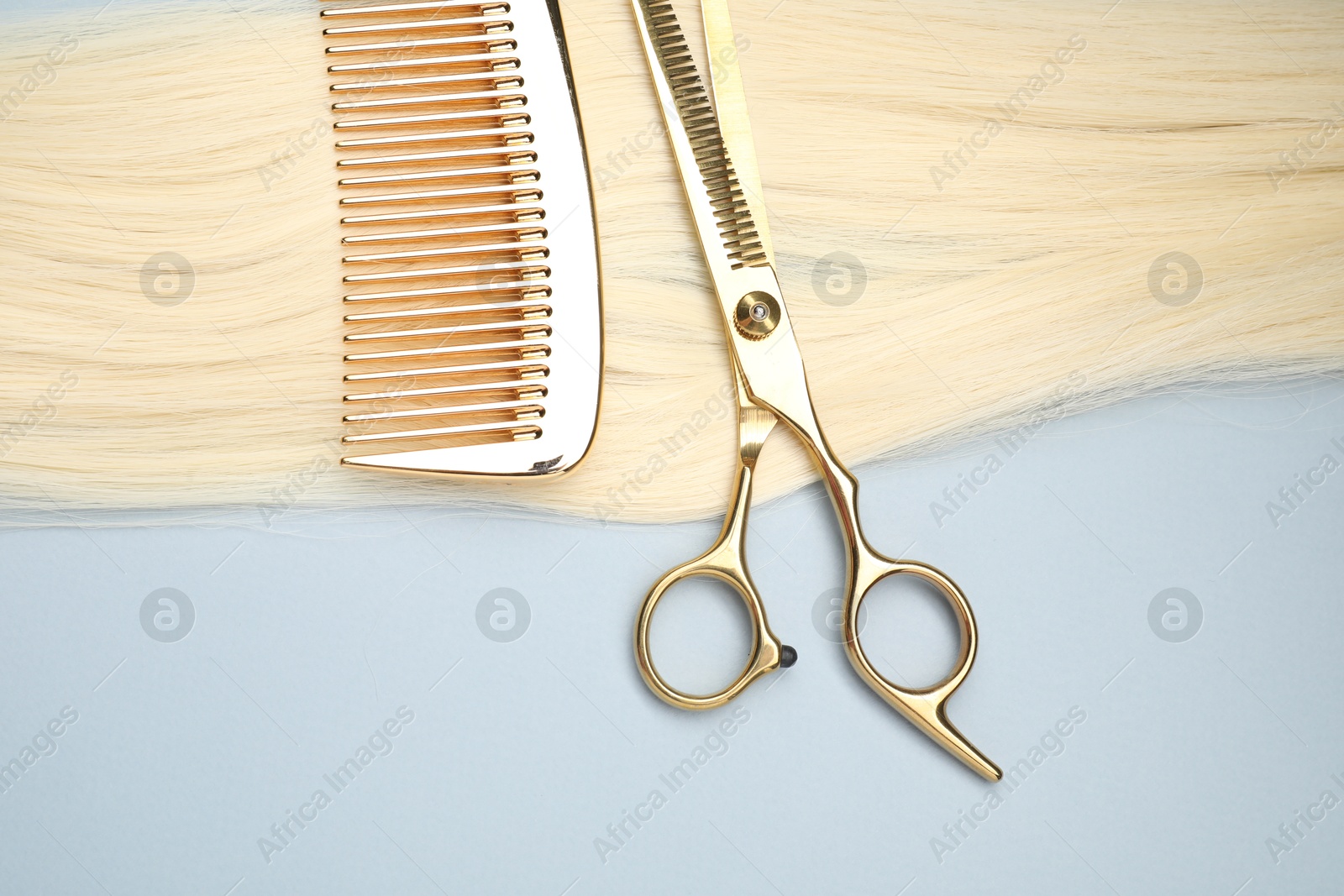 Photo of Blonde hair strand, comb and professional scissors on light grey background, top view